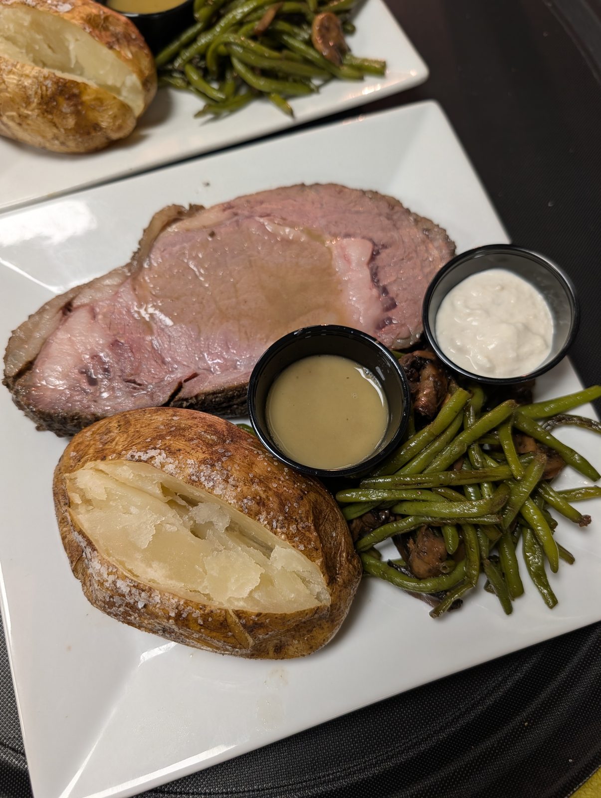 Slow-roasted prime rib with a salted baked potato, green beans, au jus, and horseradish cream
